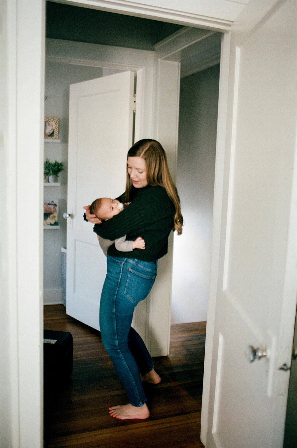 woman holds baby while standing in houses hallway